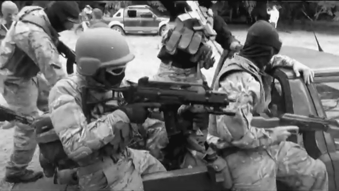 The picture shows a group of men in military uniforms sitting on the back of a truck, holding what appear to be assault weapons, or realistic airsoft replicas.